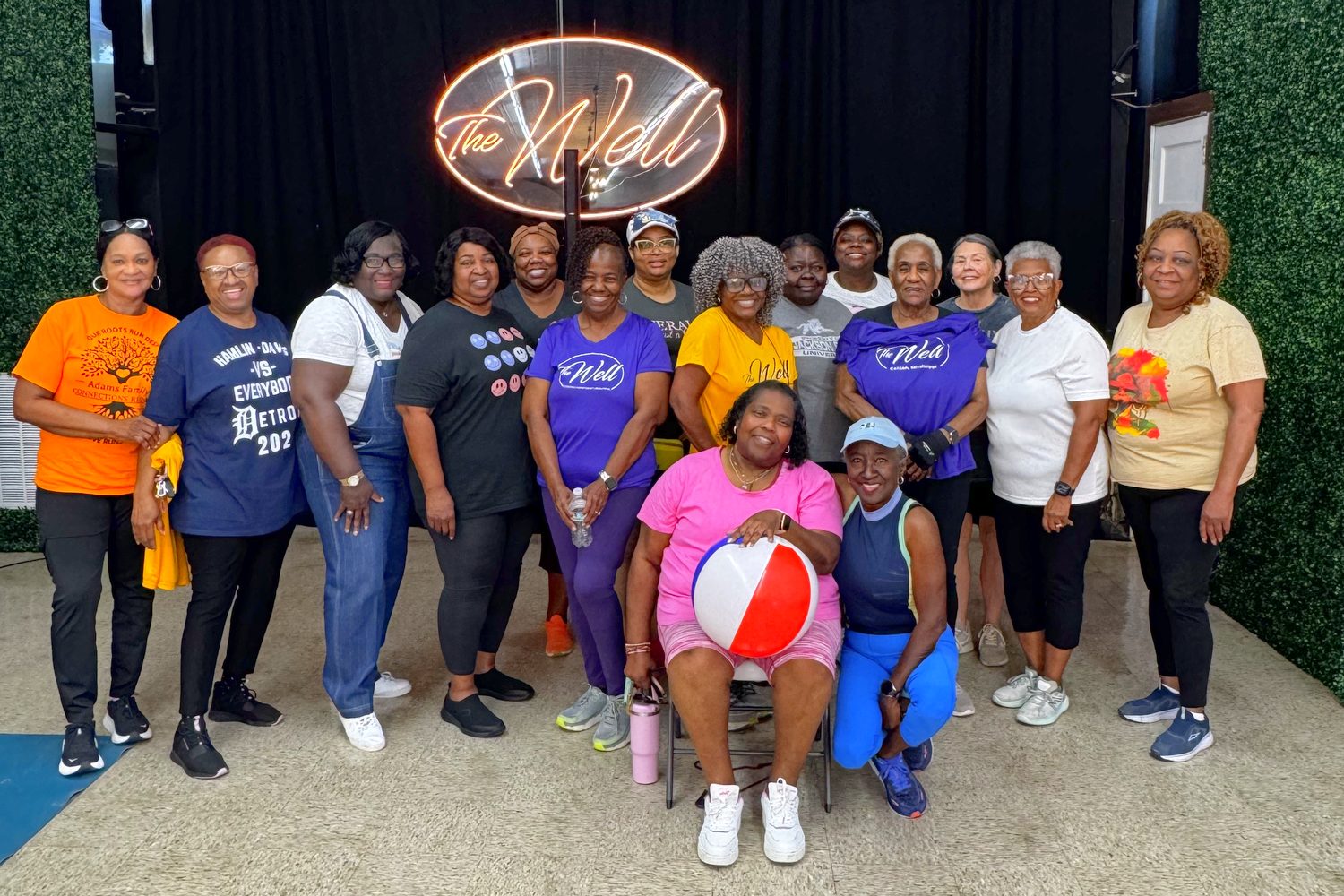 The Sit & Get Fit group smiling together under The Well's neon sign